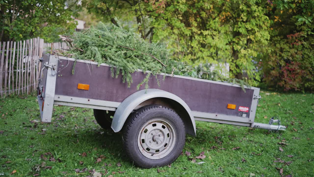 A trailer parked in a traditional German garden, filled with tree and shrub cuttings, showcasing seasonal garden cleanup and maintenance