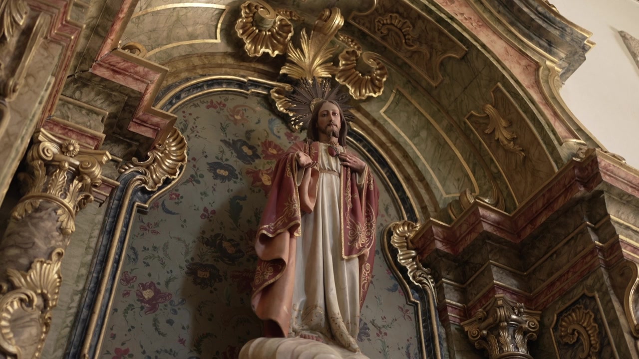 Detailní socha Ježíše v bohatě zdobeném kostelním výklenku, obklopená složitými zlatými a mramorovými akcenty.