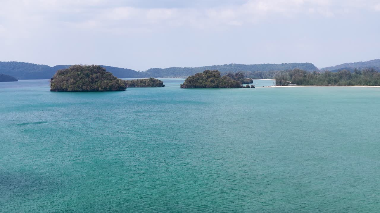 明るい日差しの下、ターコイズブルーの海と石灰岩のカルスト地形の島々を捉えた広大な空撮。