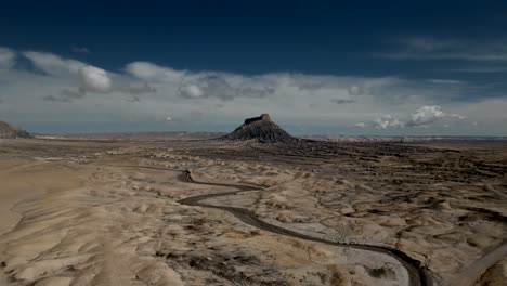 A-muddy-riverbed-winds-its-way-toward-Factory-Butte-in-the-vast-desert-landscape---aerial-approach