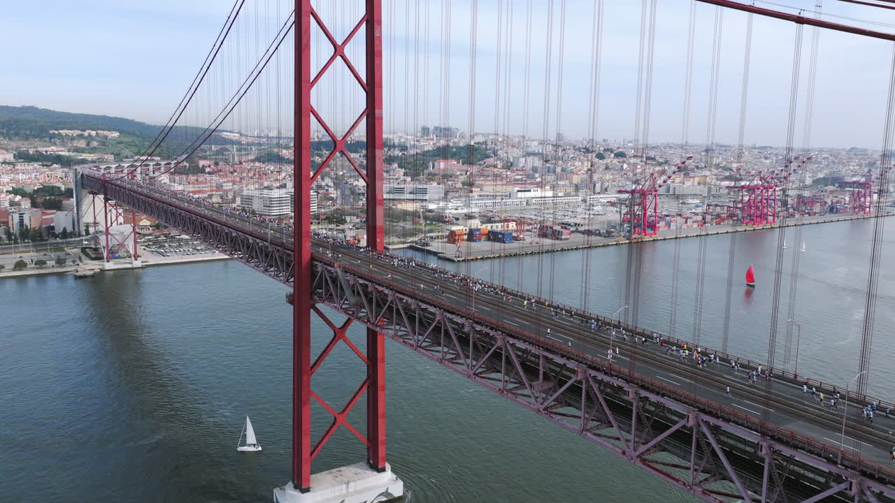 Half marathon and 10K long distance running event in Lisbon, Portugal, Europe. Runners crossing the iconic famous red 25th April suspension bridge. Aerial drone shot over the Tagus river