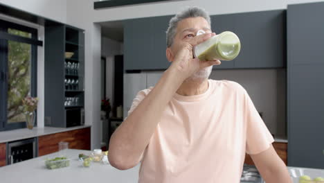 senior biracial man drinking healthy smoothie in kitchen at home, copy space, slow motion