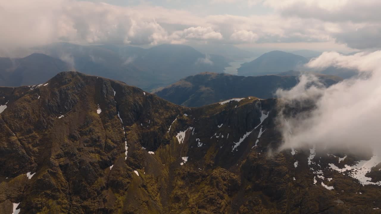 Aerial drone footage of Bidean Nam Bian, the highest mountain in Glencoe, Scotland, covered in snow. Sweeping views of snowy peaks, deep valleys, and dramatic Highland scenery