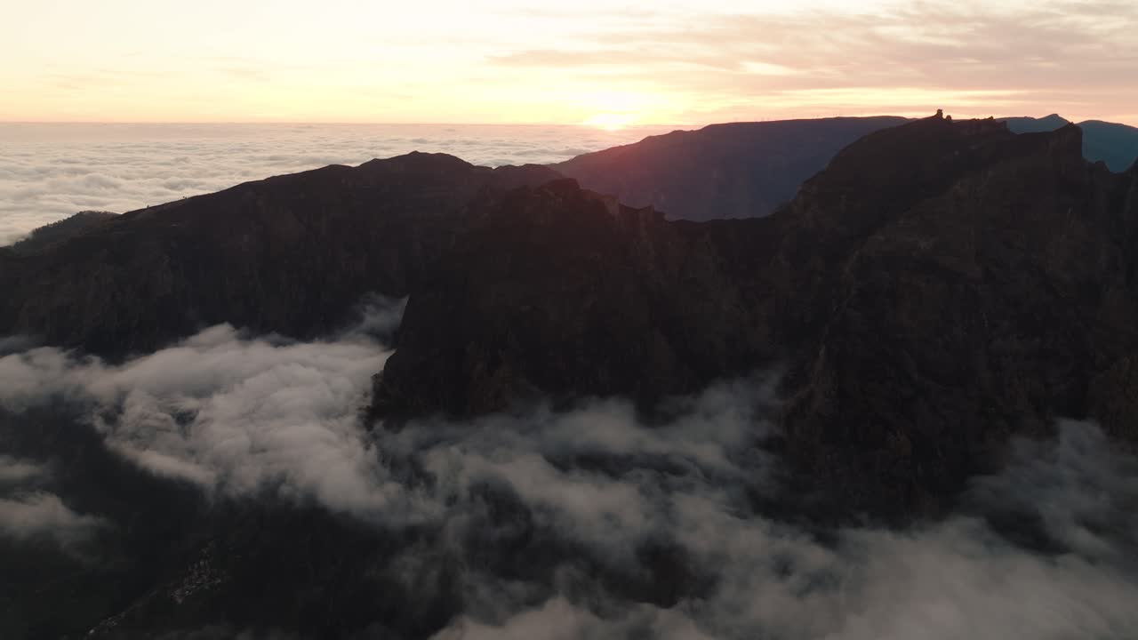 Aerial view of Pico do Arieiro’s jagged cliffs at sunset, with low clouds drifting through steep mountain valleys.