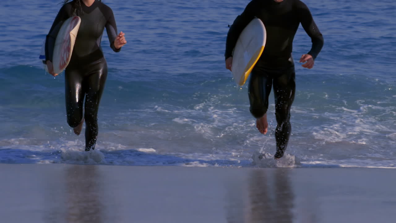 Kolme iloista surffaajaa juoksee merestä