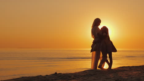 Mama-Und-Tochter-Freuen-Sich-Auf-Einen-Wunderschönen-Sonnenuntergang-über-Dem-Meer-Silhouetten-Einer-Frau-Mit