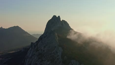 drone flight over the top of a mountain where trees grow and fog creeps on an autumnal sunny day aerial shot