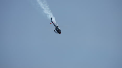 aerobatic stunt helicopter executing a vertical flip in clear blue sky with visible smoke trail