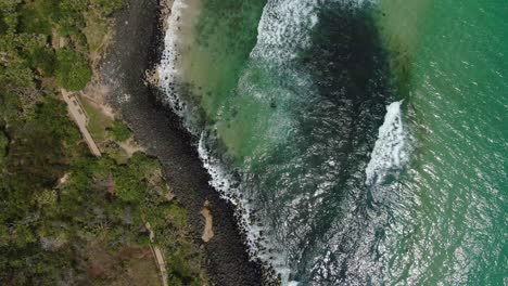 looking vertically at small waves breaking on rocky beach slight spin, bright summers day, drone