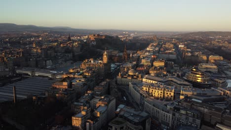 drone captures edinburgh skyline in soft golden light with historic architecture, distant hills, busy streets, railway station, and famous landmarks in calm evening atmosphere across scotland