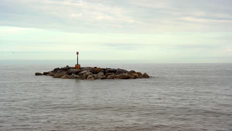 Small-rocky-breakwater-island-with-marker-post-protecting-the-coast-at-Sidmouth-in-Devon,-England