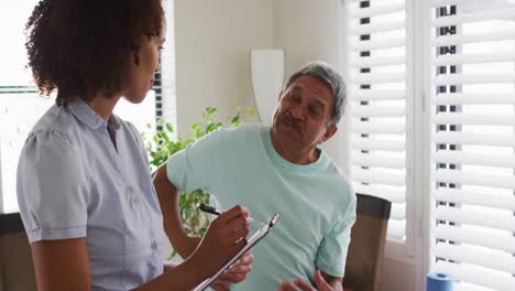 mixed race female physiotherapist talking to senior man holding his back