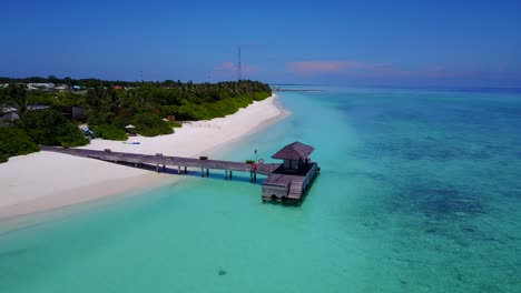 Ein-Blick-Auf-Ein-Resorthotel-Und-Seine-Holzterrasse-Auf-Dem-Türkisfarbenen-Meer-Auf-Den-Malediven,-Drohnenaufnahmen-Mit-Kreisförmigen-Bewegungen-An-Einem-Klaren-Tag