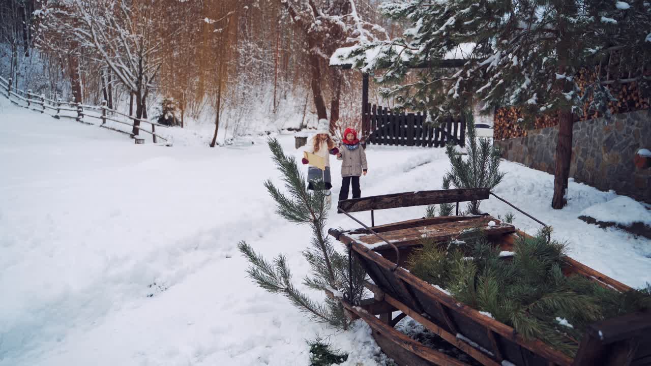Happy children with envelope in winter in the yard. Two little kids coming to old wooden sledges and brown sheep on the snowy background.