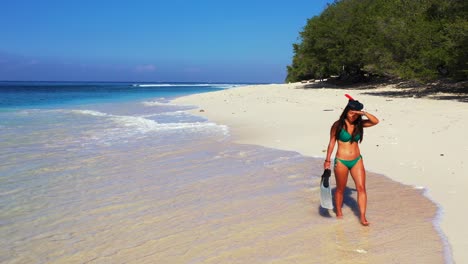 girls with snorkel mask and fins walking along sandy beach, searching for ideal place to dive into blue sea, bali