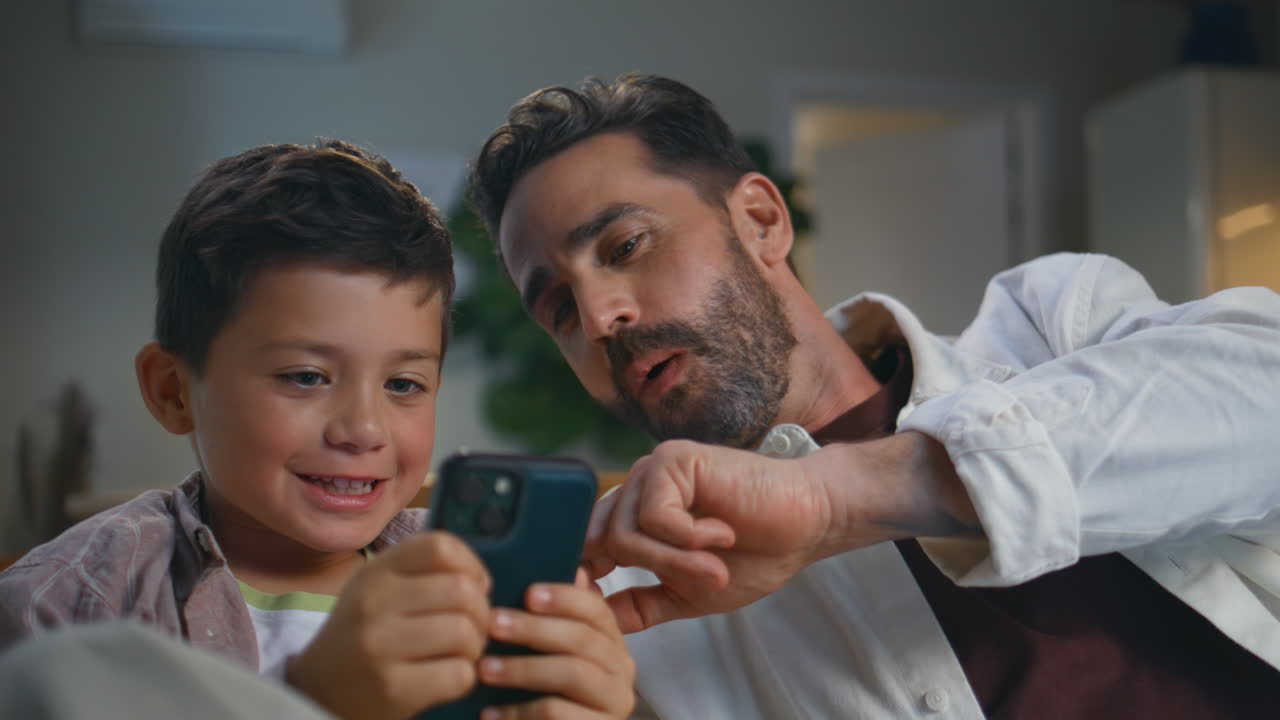 Serious boy playing mobile phone resting sofa closeup. Funny father looking son