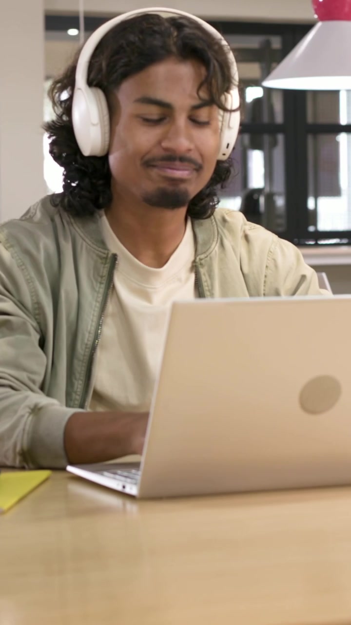 Vídeo vertical: Homem de jaqueta entrando no escritório, atendendo uma chamada, colocando fone de ouvido e ligando o laptop para trabalhar