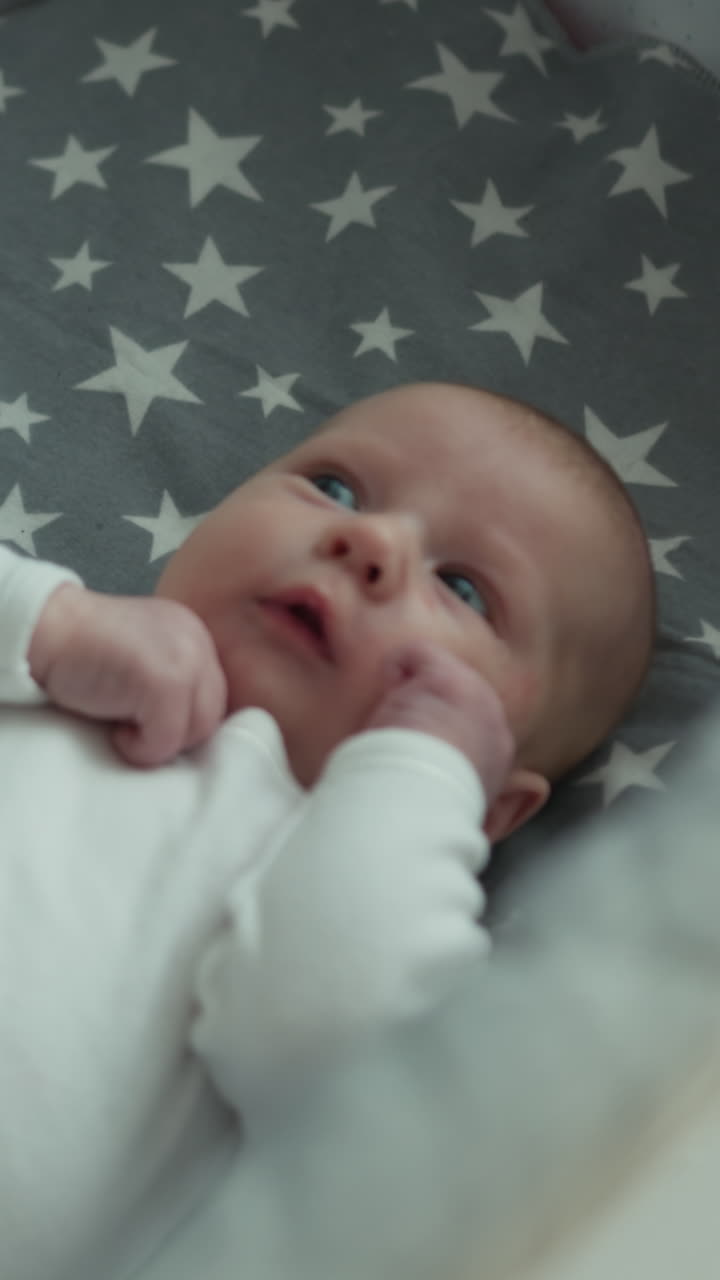 Primo piano di un neonato tranquillo che riposa su una coperta grigia adornata con stelle bianche, mostrando le sue piccole fattezze.