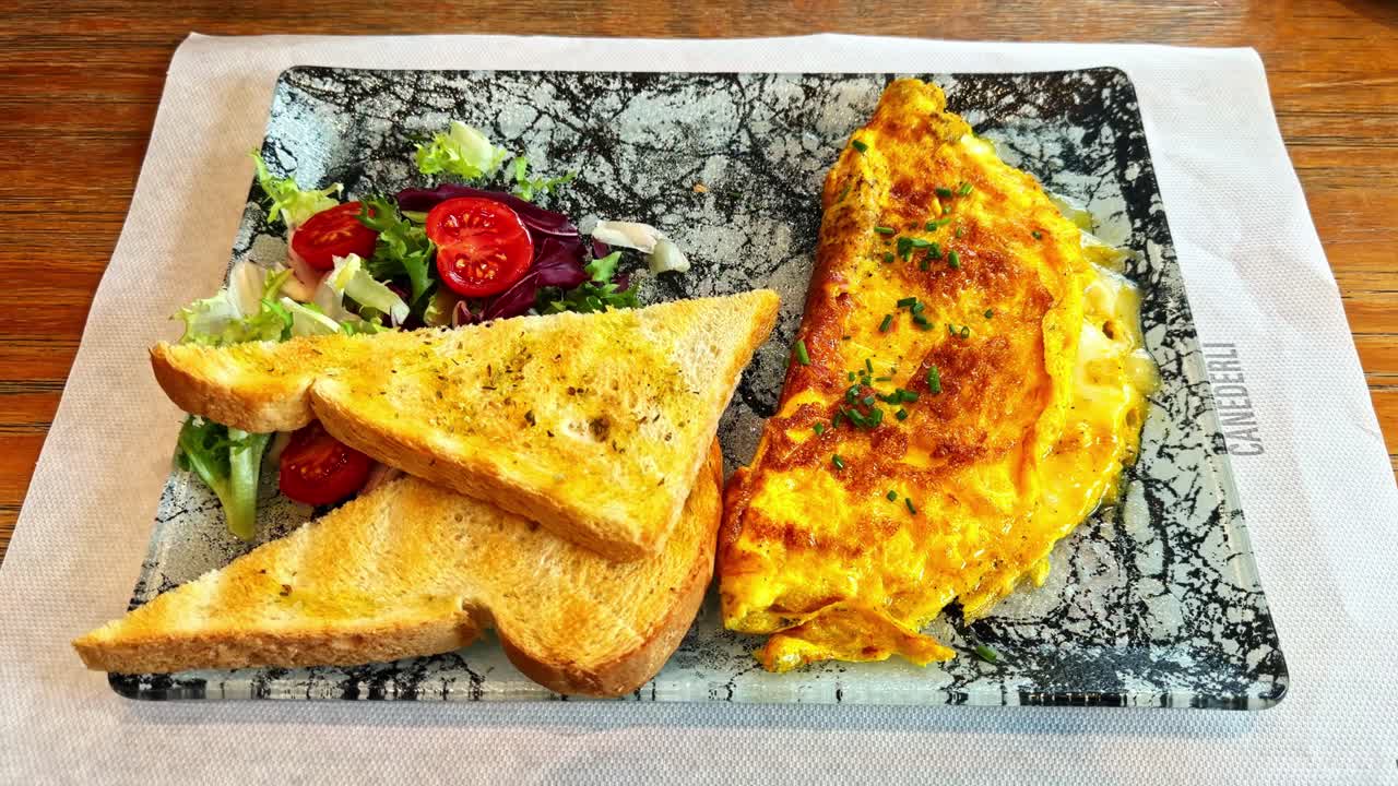 Primo piano di un'omelette al formaggio dorata servita con pane tostato e un'insalata fresca di contorno con pomodorini. Piatto per un pranzo informale in un accogliente ambiente di ristorante.