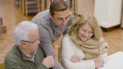 senior man and woman studying with teacher in library