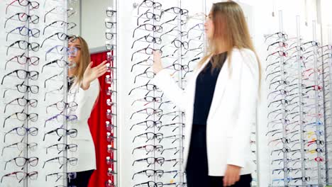 girl in new glasses looking at camera at optics. attractive young woman trying on fashionable eyeglasses indoors. happy buyer choosing spectacles.