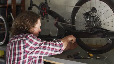 hombre caucásico enfocado reparando bicicleta usando herramientas en el garaje
