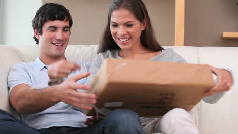 una pareja sonriente desempaquetando un regalo.