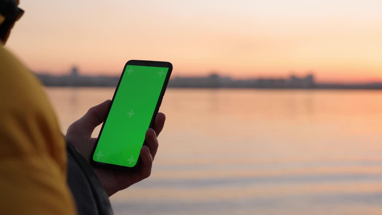 Man using green screen in smartphone near river
