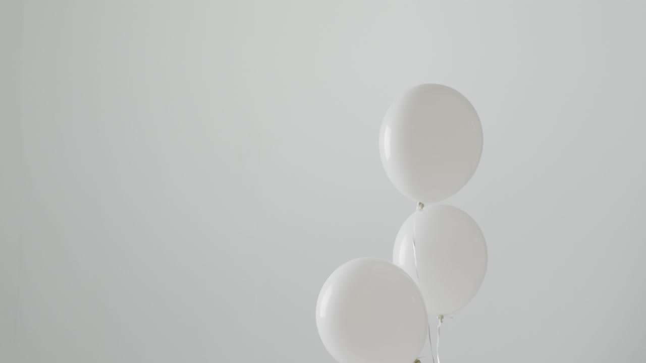 Video of three white balloons on white strings floating on white background, with copy space