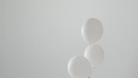 video of three white balloons on white strings floating on white background, with copy space