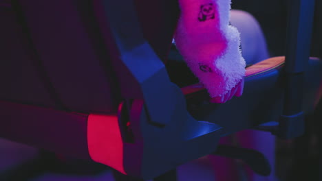 close up of hand in fluffy sweater adjusting reclining lever on gaming chair illuminated by neon pink and blue lights, showcasing ergonomic design and cozy comfort in modern indoor setting