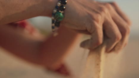 A-close-up-slow-motion-shot-of-a-Caucasian-female-lifting-up-a-handful-of-beach-sand-before-allowing-the-grains-of-sand-to-slowly-fall-through-her-fingers-on-a-sunny-day