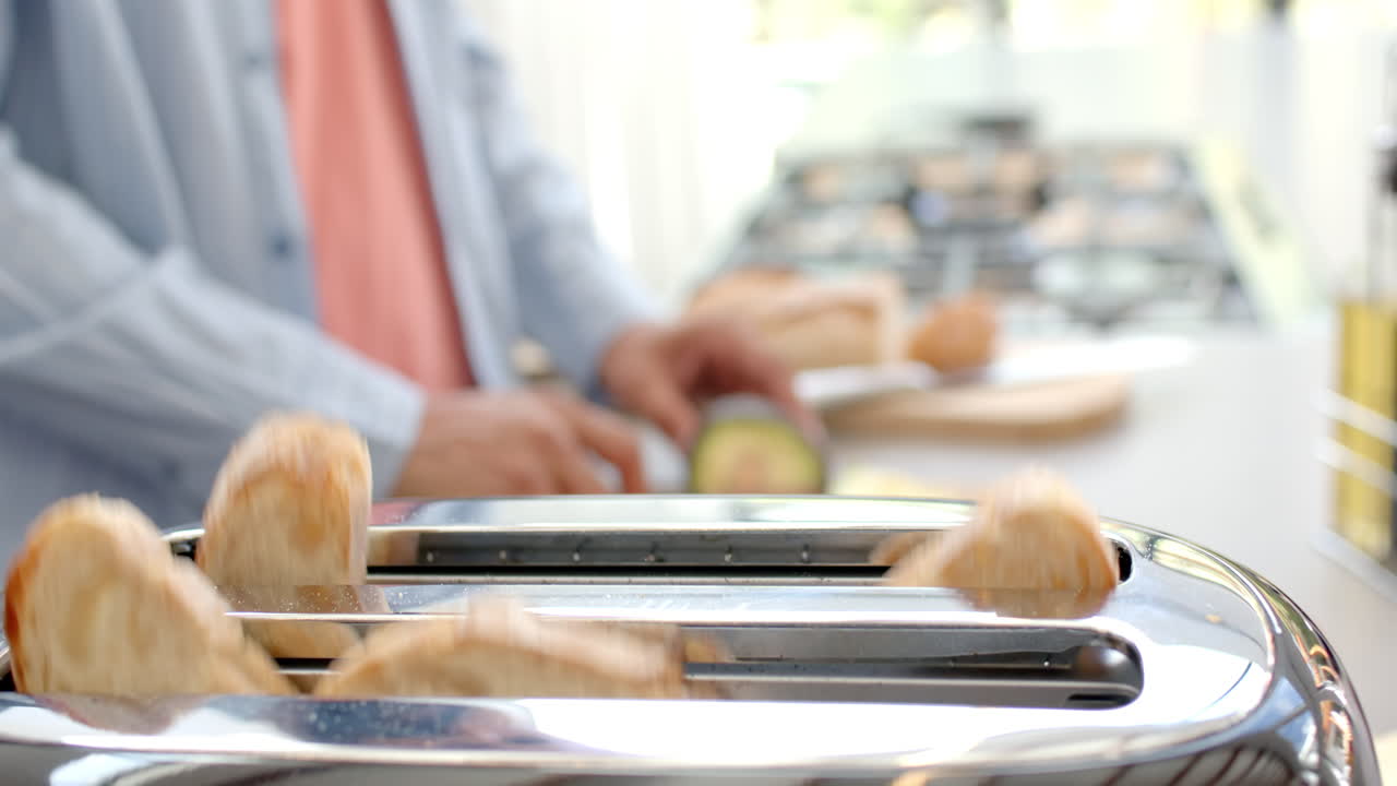 Preparing breakfast, man slicing avocado in kitchen with toaster in foreground