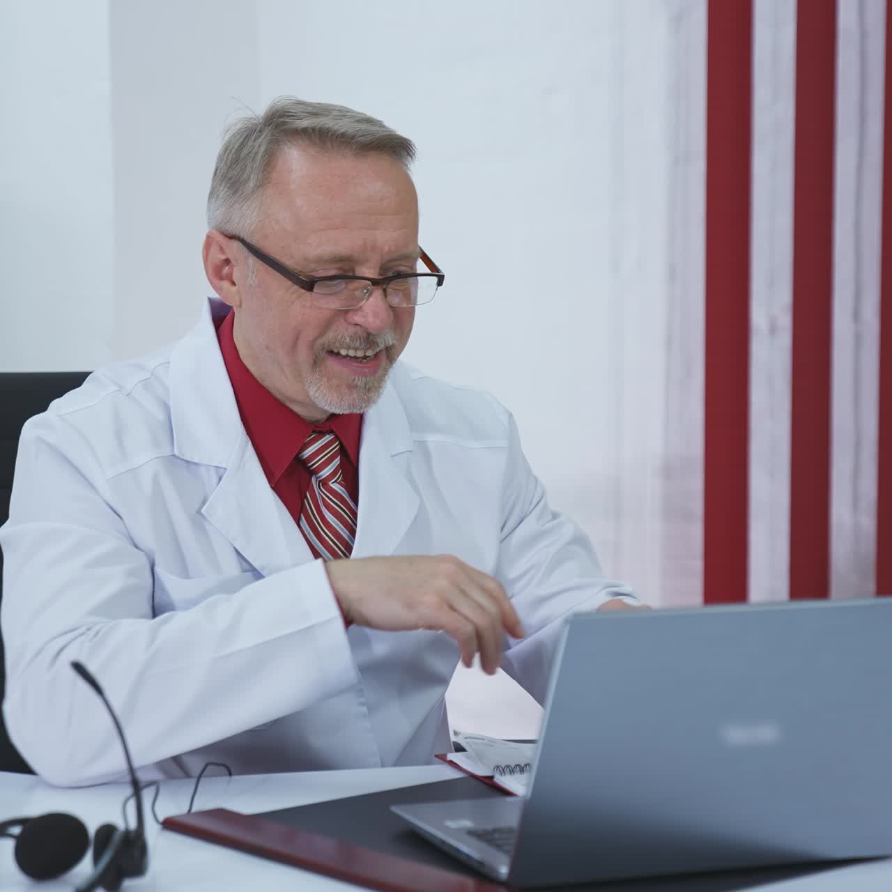 Doctor starts video call. Old professional physician putting on headphones during remote consultation in medical center. Distant medicine during quarantine.