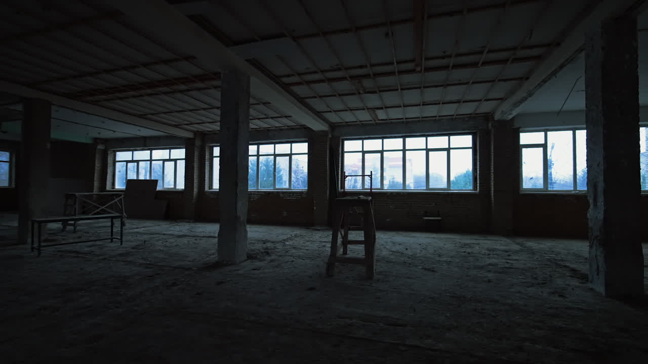 Spacious premise in the unfinished building. Some scaffolds are in the room with big windows.