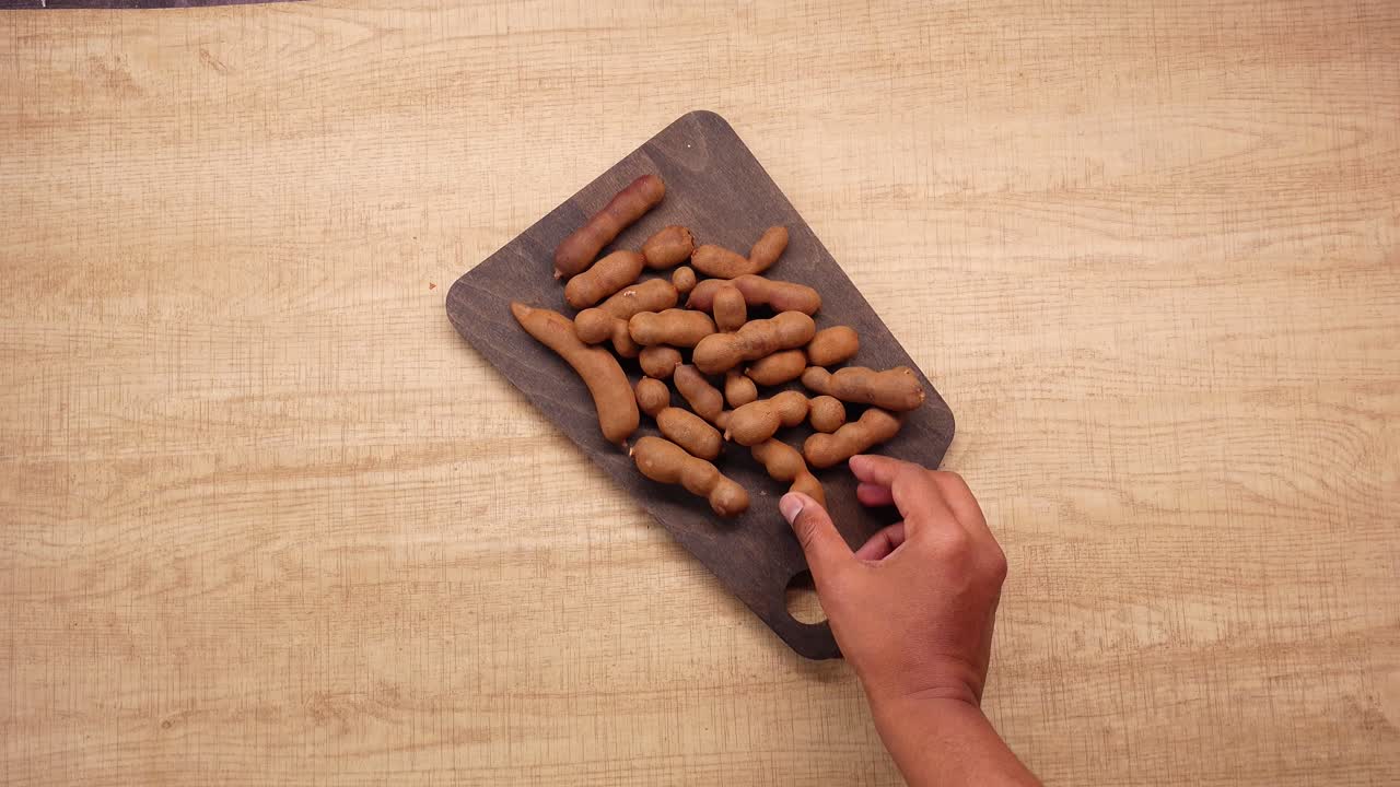 Mano che raccoglie baccelli di tamarindo freschi da una tavola di legno