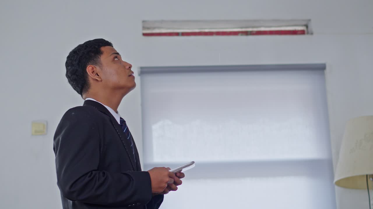 Businessman in black suit looking up at leaking ceiling with frustrated expression