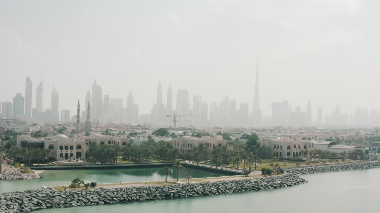 Jumeirah area and Dubai towers silhouette in background, hot afternoon, Pan aerial