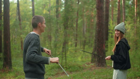 brother and sister smile warmly while playing together in forest using tent poles, enjoying nature and bonding in outdoor campsite surrounded by tall trees and greenery on peaceful sunny day