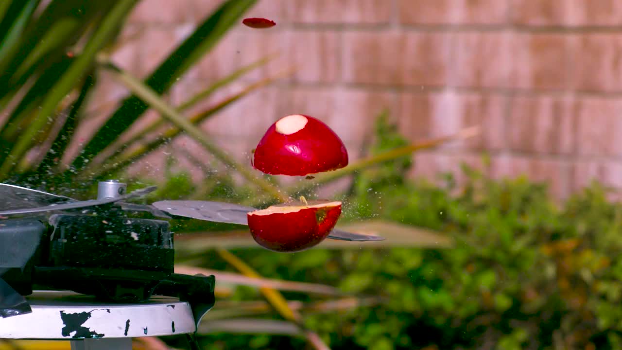 빨간 사과가 느린 속도로 회전하는 금속 칼날에 의해 은 조각으로 잘라지는 동안 사과가 위로 날아가서 씨과 주스를 방출합니다.
