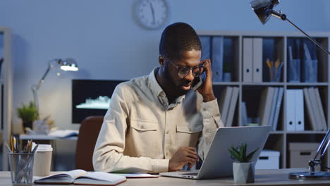 office worker sitting at the laptop having not pleasant phone conversation in the office at night