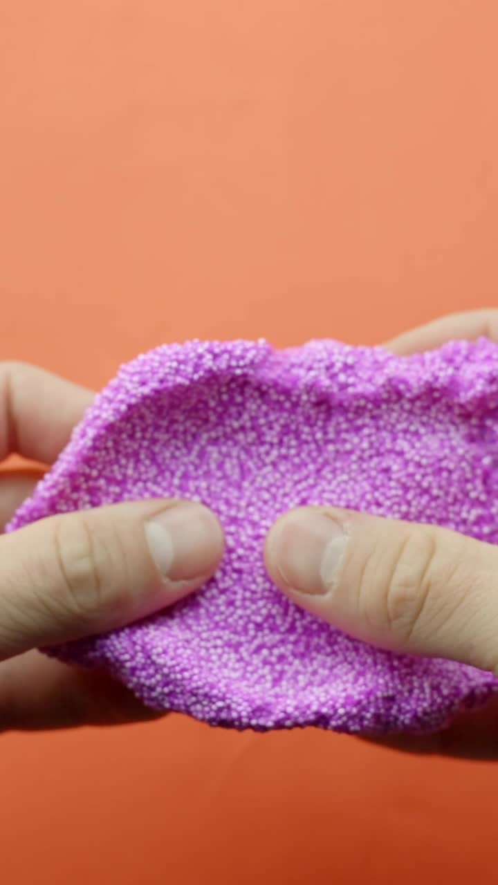 Hands stretch pink floam against orange background, playful texture, vertical