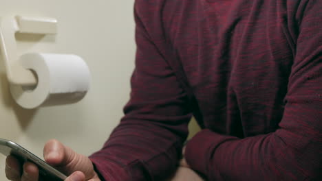 Man-uses-mobile-phone-while-sitting-on-the-toilet