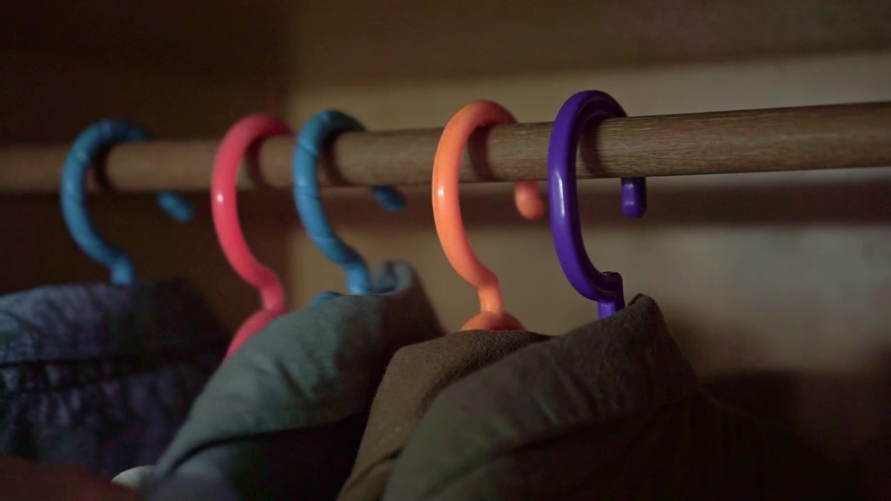 Primer plano de perchas de ropa coloridas en una barra de armario de madera, mano seleccionando ropa del guardarropa, concepto de rutina matutina y elección de moda