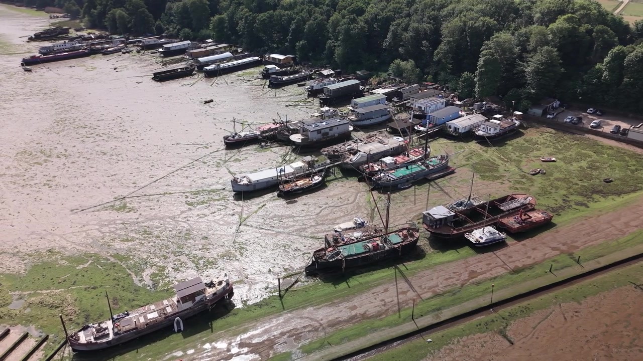 Luftfoto af fortøjede både og pramme ved lavvande langs en skovklædt kystlinje i Suffolk.