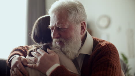 senior man hugging young granddaughter and talking to her at home