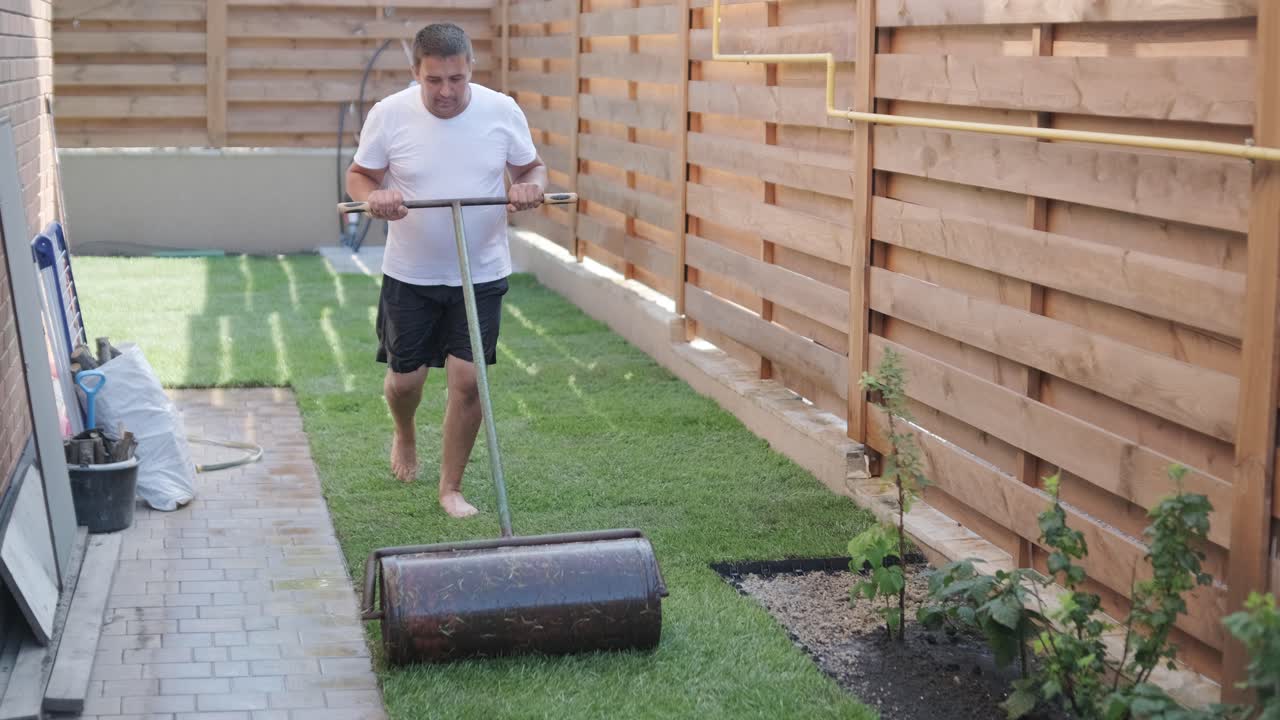 Tukang Kebun Memasang Rumput di Halaman Pribadi dengan Pagar Kayu