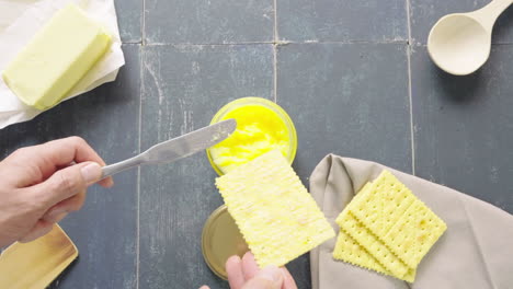 man's hand puts ghee butter on a soda cracker and drops knife on top of the pot