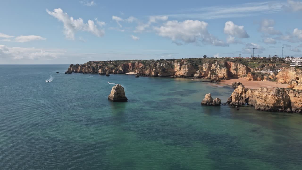 Un dron aéreo se aleja y se inclina hacia abajo, revelando aguas turquesas, formaciones de piedra caliza, playas de arena e impresionantes acantilados anaranjados a lo largo de la costa del Algarve en Portugal, cerca de Lagos.
