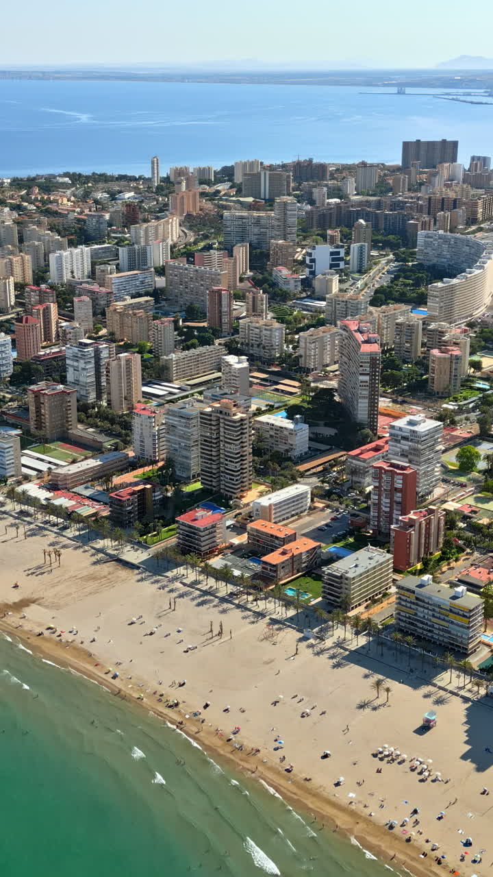 Aerial drone view of the buildings along the coastline with people relaxing on the beach in Alicante, Spain in daylight. Vertical